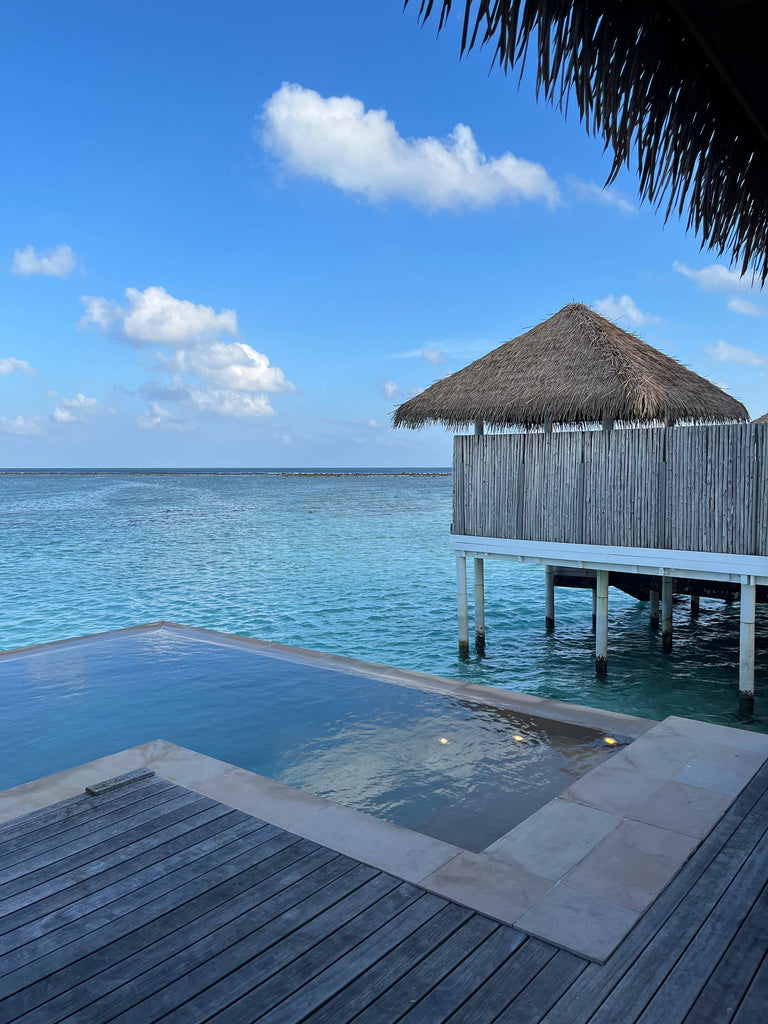 infinity pool by ocean with nearby bungalow hut and scattered clouds in sky