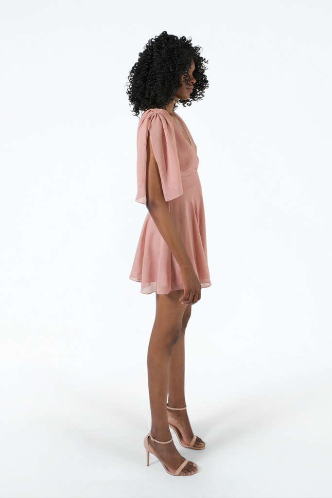 Side view of pink silk crinkle short dress, fitted at waist, flared hem, ruffled sleeves scrunched up to shoulder with drawstring, worn with pink heels 