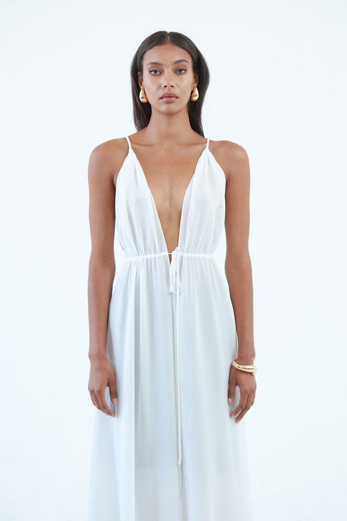 long white silk dress with thin shoulder straps, and full length front slit secured by waist tie.