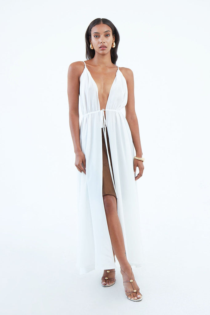long white silk dress with thin shoulder straps, and full length front slit secured by waist tie, worn as beach cover up.