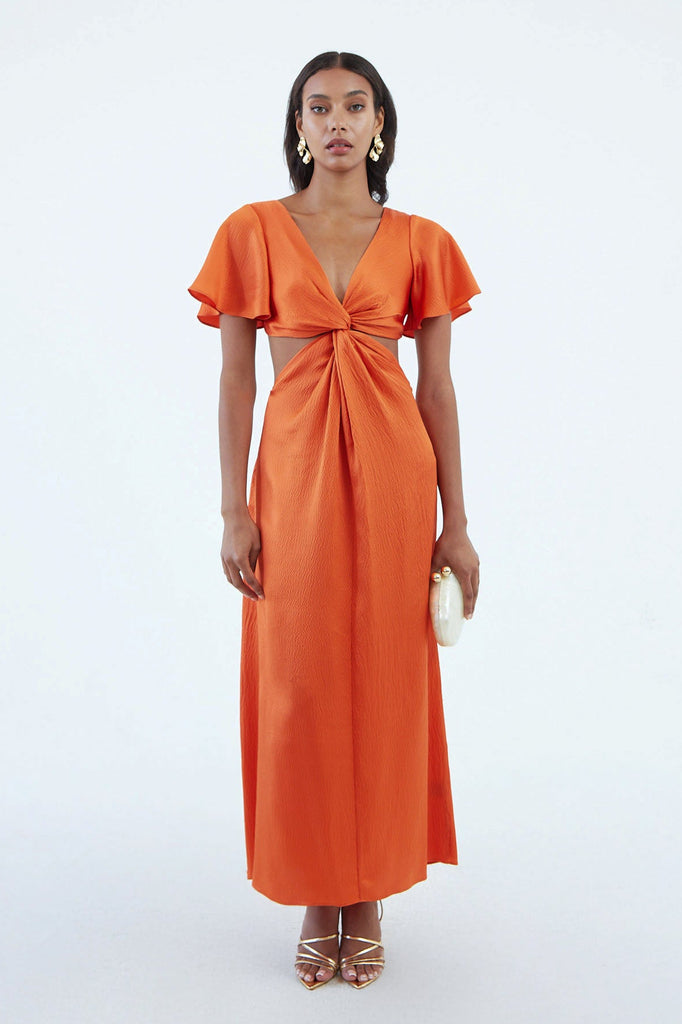 Long orange silk dress with flared short sleeves, low V neck, and a center twist with exposed waist side, worn with gold sandals