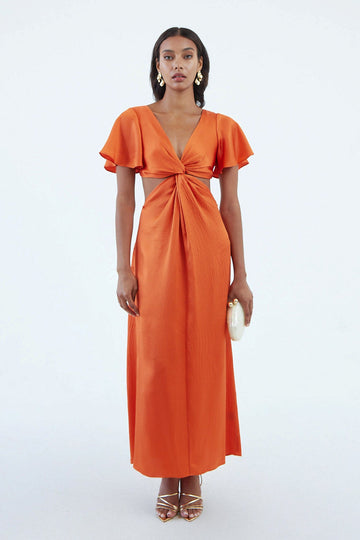 Long orange silk dress with flared short sleeves, low V neck, and a center twist with exposed waist side, worn with gold sandals