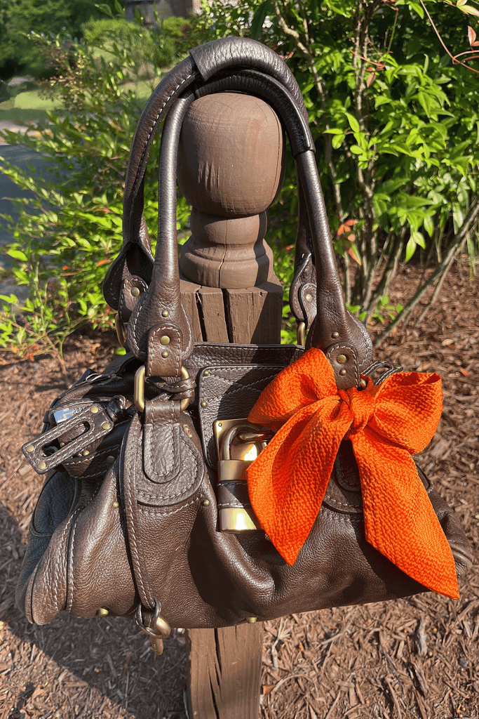 orange silk tie in bow used as purse charm on a dark brown leather bag with brass