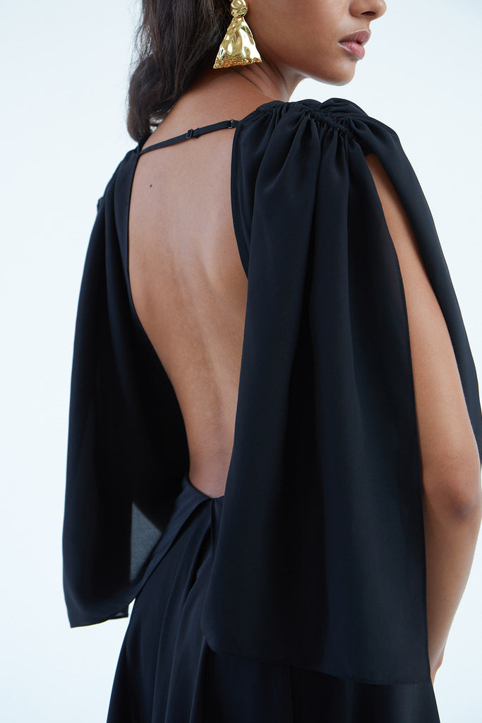 open back black silk wrap dress with back shoulder blade strap, wide sleeves, and asymmetrical hem, worn with gold earrings