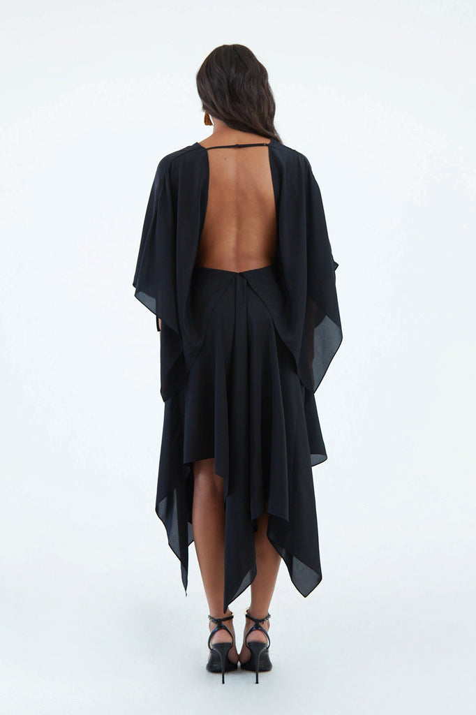 open back black silk wrap dress with back shoulder blade strap, wide sleeves, and asymmetrical hem, worn with black high heels and red earrings